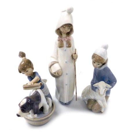 Three Lladro porcelain figures, comprising a girl kneeling with a lamb, standing girl with basket, and a kneeling girl washing a hound in a washtub. (3)