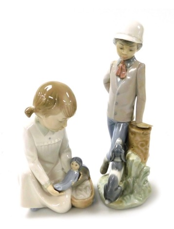 A Nao porcelain figure of a boy, modelled standing with a puppy looking up at him, and a further Nao figure of a girl placing her doll into a pram. (2)