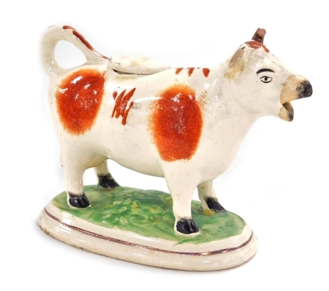 A late 19thC pottery cow creamer, with red markings, raised on an oval base, 17cm wide. (AF)