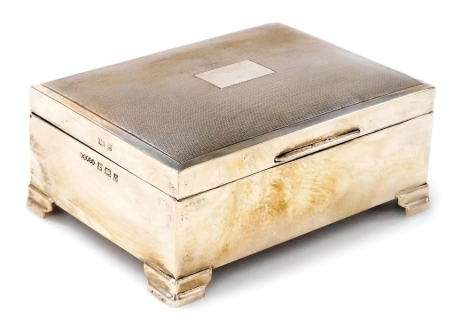 An Elizabeth II silver cigarette case, the lid with engine turned decoration and vacant cartouche, raised on four stepped feet, Harman Bros., Birmingham 1958, 11cm wide.