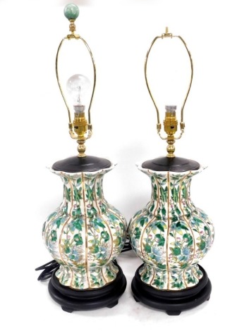 A pair of Chinese porcelain famille verte table lamps, of fluted baluster form, decorated with panels of flowers and leaves, raised on circular wooden bases, 70cm high. Buyer Note: WARNING! This lot contains untested or unsafe electrical items. It is supp