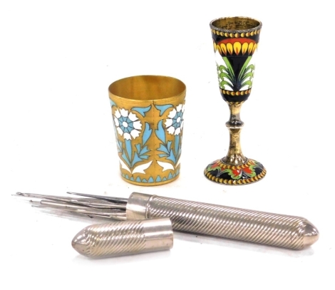 An early 20thC Russian gilt metal tot, with enamelled decoration in white and turquoise of repeating flowers, impress mark, 5.5cm high, a Russian champleve enamel and silver cup, decorated with stylised flowers, 9.5cm high, and a plated crochet hook case 