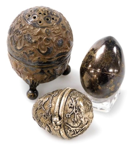 A Georgian silver thimble holder, of egg form, hallmarks indistinct, together with an Indian white metal pepperette embossed with figures, and a further white metal egg embossed with birds and blossom. (3)