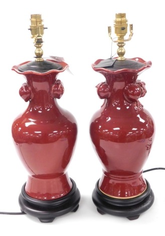 A pair of Chinese sang-de-boeuf vase form table lamps, of baluster form, with fruit moulded handles, raised on wooden socle bases, 51cm high. Buyer Note: WARNING! This lot contains untested or unsafe electrical items. It is supplied for scrap or recondit