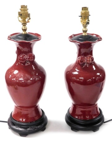 A pair of Chinese sang-de-boeuf vase form table lamps, of baluster form, with fruit moulded handles, raised on wooden socle bases, 51cm high. Buyer Note: WARNING! This lot contains untested or unsafe electrical items. It is supplied for scrap or recondit