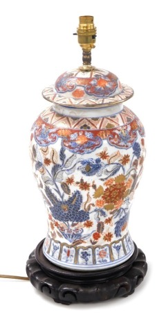 A Chinese porcelain jar and cover table lamp, of baluster form, Imari decorated with flowers and scrolling leaves, raised on a hardwood stand, 48cm high.