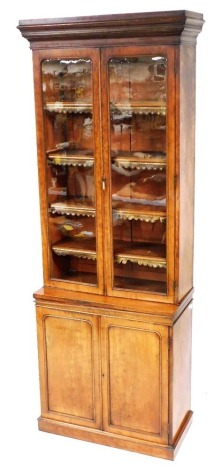 A Victorian mahogany cupboard bookcase, the out swept pediment over a pair of glazed doors enclosing four shelves, above a pair of panelled doors, on a plinth base, 245cm high, 87cm wide, 43cm deep.