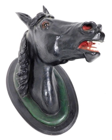 A late 19thC plaster horse's head, painted in black, raised on a oval ebonised mount, 63cm high, 65cm wide.