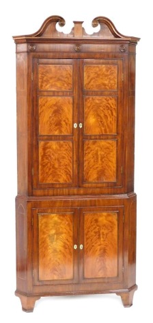 A George III mahogany standing corner cupboard, with a swan neck pediment, over a pair of panelled doors, enclosing three shaped shelves, above a further pair of doors, enclosing a single shelf, raised on bracket feet, 242cm high, 103cm wide, 53cm deep.