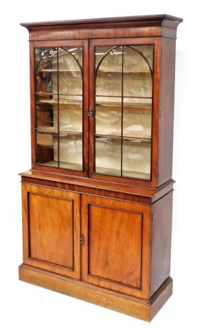 A Victorian mahogany cupboard bookcase, the outswept pediment over a pair of astragal glazed doors enclosing three shelves, over a pair of panelled doors enclosing further shelf, raised on a plinth base, 218cm high, 121cm wide, 46cm deep.