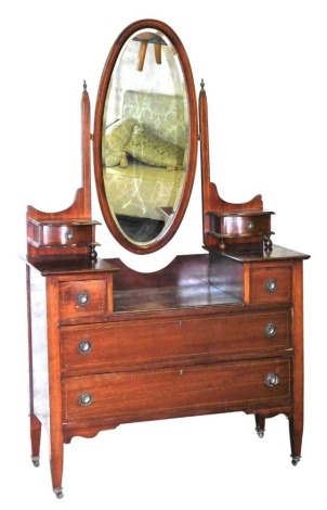 An Edwardian mahogany dressing chest, the superstructure with an oval swing frame mirror inset bevelled glass, flanked by two small drawers, over two square above two long drawers, raised on tapering square legs, brass capped on castors, 177cm high, 105cm