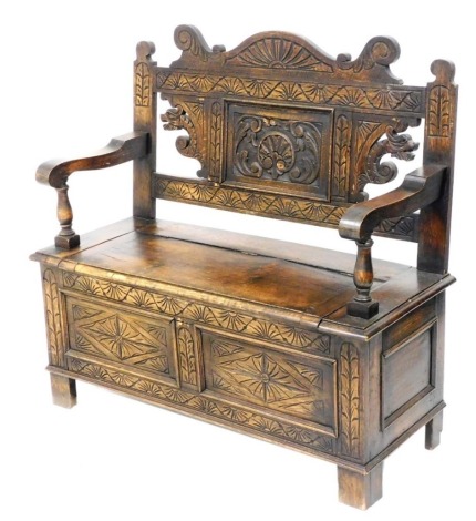 An early 20thC carved oak settle, with a scroll and panelled back, carved with leaves, flowers and dragons, the seat with lift up lid, above a pair of panels foliate carved, raised on stiles, 106cm wide.