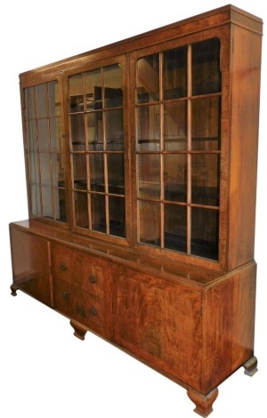 An early 20thC walnut library bookcase, the pediment over three doors, each enclosing three shelves, over two frieze drawers flanked by cupboards, raised on ogee bracket feet, 199cm high, 212cm wide, 51cm deep.