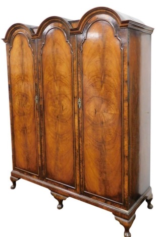 An early 20thC walnut triple wardrobe, with a triple domed pediment, over two doors, enclosing a hanging rail, flanked to the left by four shelves over two frieze drawers, raised on cabriole legs, 195cm high, 159cm wide, 56.5cm deep.