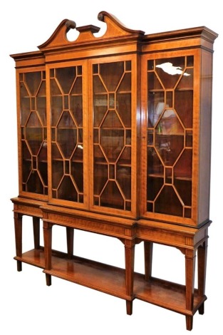 An Edwardian mahogany and line inlaid break front bookcase, Adam style, with a broken neck pediment, over four glazed doors, each enclosing three shelves, above a table base, raised on tapering square legs united by an under tier, 227cm high, 183cm wide, 