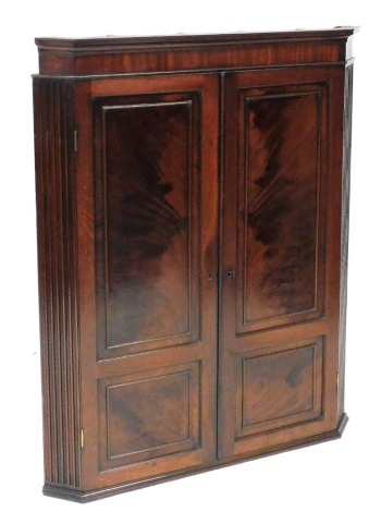 A George III mahogany hanging corner cabinet, the pediment over a pair of panel doors enclosing three serpentine shaped shelves, raised on a plinth base, 118cm high, 92cm wide, 53cm deep.