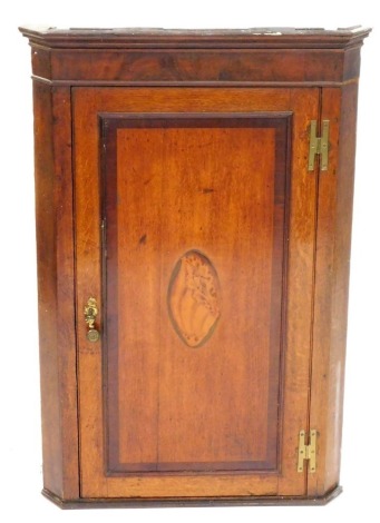 A George III mahogany and rosewood cross banded wall hanging corner cupboard, the outswept pediment over a single door with shell paterae inlay, opening to reveal three serpentine shelves, raised on a plinth base, 103cm high, 68cm wide, 39cm deep.