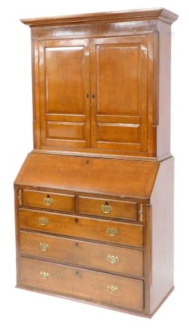 A George III oak bookcase bureau, the out swept pediment over a pair of panelled doors enclosing two adjustable shelves, above a fall flap, resting on skivers, enclosing an arrangement of doors, drawers and recesses, above two short over three long gradua