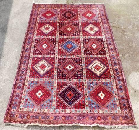 A Persian Quashqai red ground rug, decorated with fifteen floral medallions, within repeating floral borders, 305cm x 195cm.