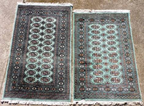 A pair of Bokhara turquoise ground rugs, decorated with a central rectangular panel with twenty-two medallions, and other motifs, within repeating floral borders, 160cm x 96cm.