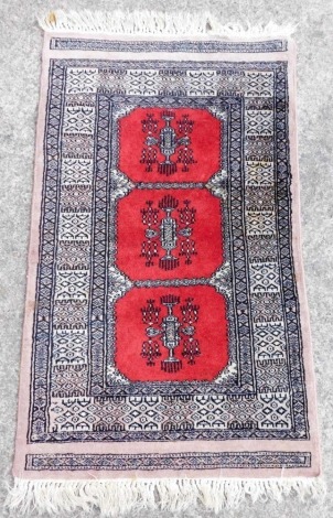 A Bokhara red ground prayer rug, with three central motifs, within repeating geometric borders, 98cm x 58cm.