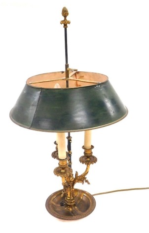 An early 20thC Continental brass three branch table lamp, with a green painted tin shade, raised on a leaf enveloped column with three foliate scroll arms, above a circular base, 71cm high.