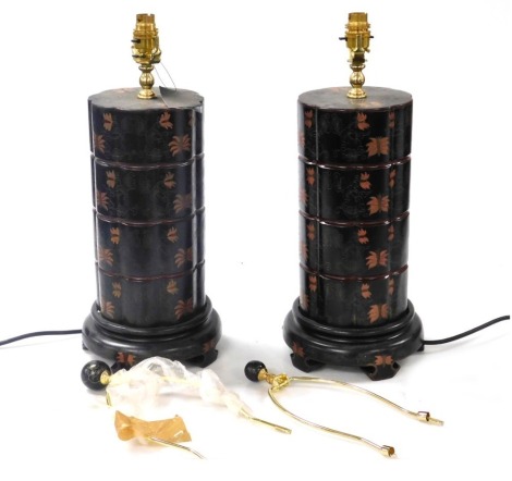 A pair of Chinese black lacquer table lamps, decorated with bands of flowers and scrolling leaves, raised on circular wooden bases, 46cm high.