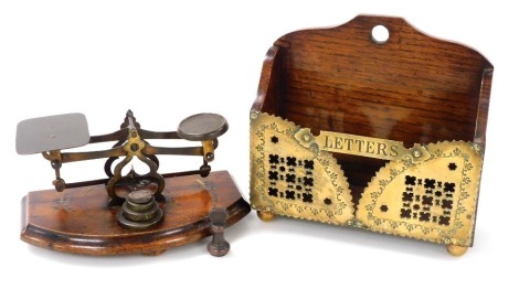 A Victorian oak and brass letter rack, raised on brass ball feet, 17cm wide, together with a set of postal scales, with weights, 17cm wide. (2)