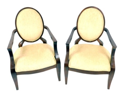 A pair of open armchairs, each with a rounded back, solid overstuffed seat, raised on splayed legs. The upholstery in this lot does not comply with the 1988 (Fire & Fire Furnishing) Regulations, unless sold to a known exporter or upholsterer it will be cu