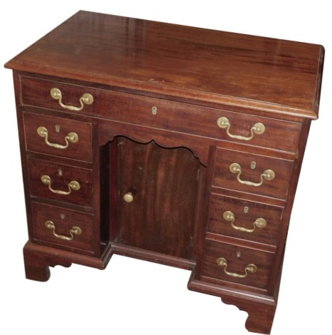 A George III mahogany kneehole dressing table or desk, the rectangular top with a moulded edge, above a frieze drawer and six small drawers around a recess with a further door, on an inverted breakfront base with bracket feet, 77cm high, 82cm wide, 50cm d