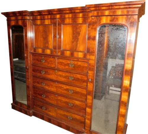 A 19thC figured mahogany inverted breakfront wardrobe, with a moulded cornice, above two panelled doors and an arrangement of two short and four long drawers, each with pierced brass drop handles, flanked by two mirrored full length doors, on a plinth, 20