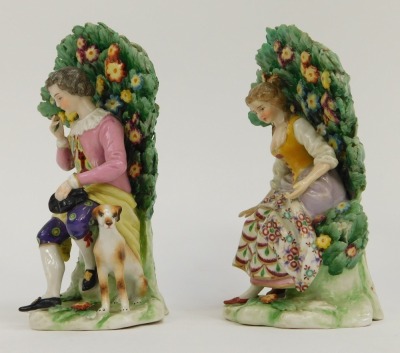 A pair of Continental Derby style porcelain figure groups, of lady and gentleman seated on perch with floral spray back, red crown stamp to underside, 15cm high. - 2