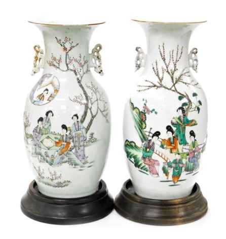 A near pair of late 19thC Qing Dynasty porcelain vases, of twin handled ovoid form, decorated with figures in a garden, 43cm high, on wooden stands.