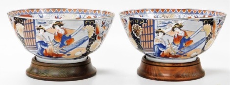 A pair of 20thC Japanese Imari bowls, decorated externally with figures on a floral ground, and on the inside with a jardiniere of flowers on a floral ground, with wooden stands, 36cm wide.