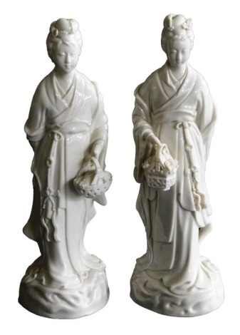 A pair of 20thC Chinese blanc de chine porcelain figures, modelled as Guanyin standing holding a basket of flowers, 26cm high.