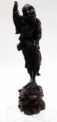 A Chinese wooden carving of an Immortal, modelled standing, his left foot upon a wild beast, on a rocky base, 46cm high (AF), together with hardwood wooden stands. (a quantity) - 2