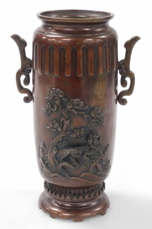 A Meiji period Japanese bronze vase, of twin handled cylindrical form, decorated in relief with a dragon, lion dog and flowers, raised on an integral base, 22cm high.