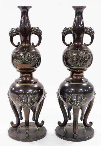 A pair of Japanese bronze vases, of twin handled baluster form, decorated in bas relief with panels of birds and dragonflies, raised on three lion's head capped cabriole legs, 21cm high.