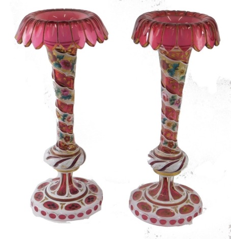 A pair of 19thC Bohemian ruby glass vases, with gilt highlighted floral tops, on turned stems, hand painted with flowers, 32cm high.