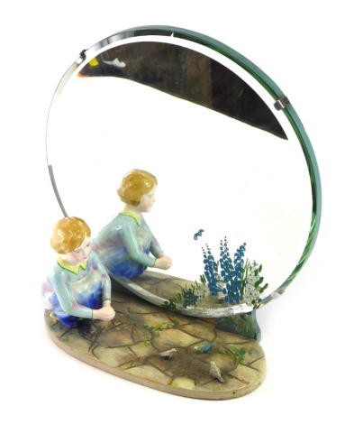 A mid 20thC freestanding mirror, with wooden easel back, fronted by a child and birds, the glass partially painted with flowers, 25cm high.