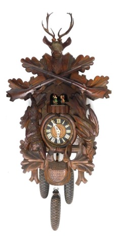 A Black Forest dancer and cuckoo clock, the pedimented case flanked by carved game, with stag finial and heavily carved leaf body, with weights and chain, 42cm high.