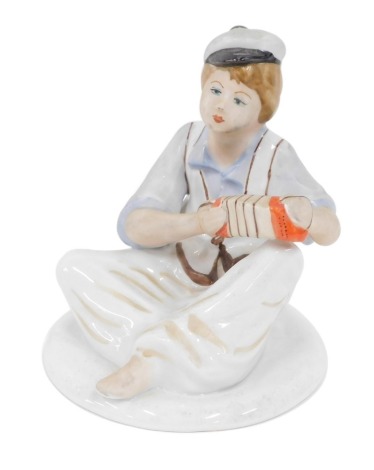 A Ukrainian Polonne porcelain figure of a child playing squeeze box, orange mark beneath, 13cm high.