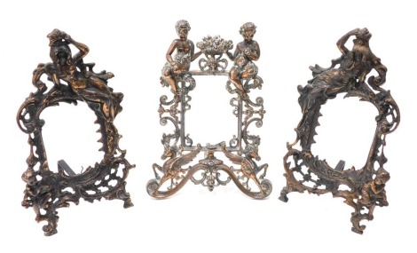 Two bronze coloured metal rococo style frames, profusely decorated with scrolls and figures, with easel backs, 32cm high, and another similar. (3)