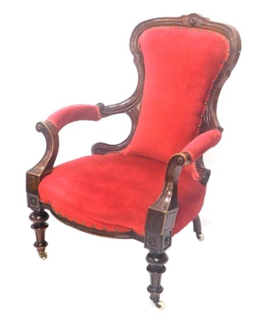 A Victorian walnut show frame open armchair, with a padded back, arm rests and seat upholstered in red fabric, on turned tapering legs with ceramic castors.