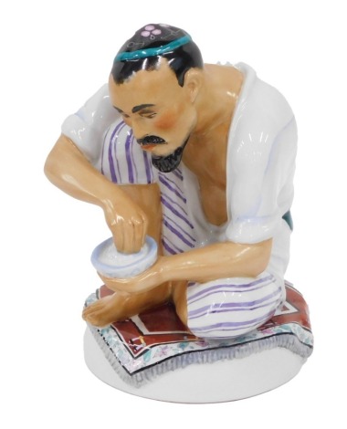 A 1920s Lomonosov Russian figure of a gentleman, crouched with bowl of rice, on a carpet, polychrome decorated, impressed hammer and sickle and printed marks in red beneath, 16cm high.