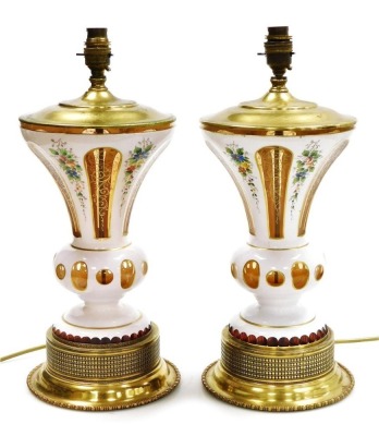 A pair of late 19thC milk flash glass vases, converted to table lamps, painted with flowers, the reserves gilt heightened, with brass fittings, 44cm high.