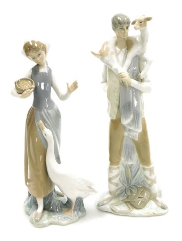 A Lladro porcelain figure of a boy with a kid goat, wrapped around his shoulders, 28cm high, and a further Lladro figure of a girl with a bowl of seeds, feeding a goose, 24cm high. (2)