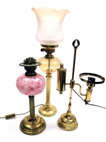 An early 20thC cranberry glass and brass oil lamp, the reservoir decorated with white opaline and aventurine, no chimney or shade, 44cm high, together with a brass oil lamp form table lamp, with an etched frosted glass shade, 66cm high, and a further bras