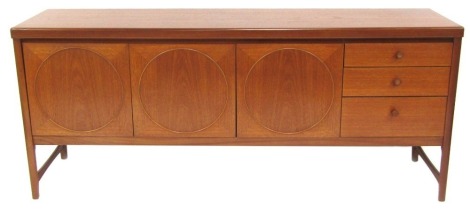 A mid century Nathan teak sideboard, the top with a rounded edge above two doors flanked by a fall, each door decorated with a raised circular design, flanked by three further drawers, on square legs united by stretchers, 77cm high, 183cm wide, 45cm deep.