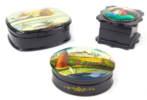 Three Russian black lacquered trinket boxes, each with a painted panel depicting various scenes, to include boat scenes signed, another of buildings marked Peaockuho, and an unmarked example. (3)